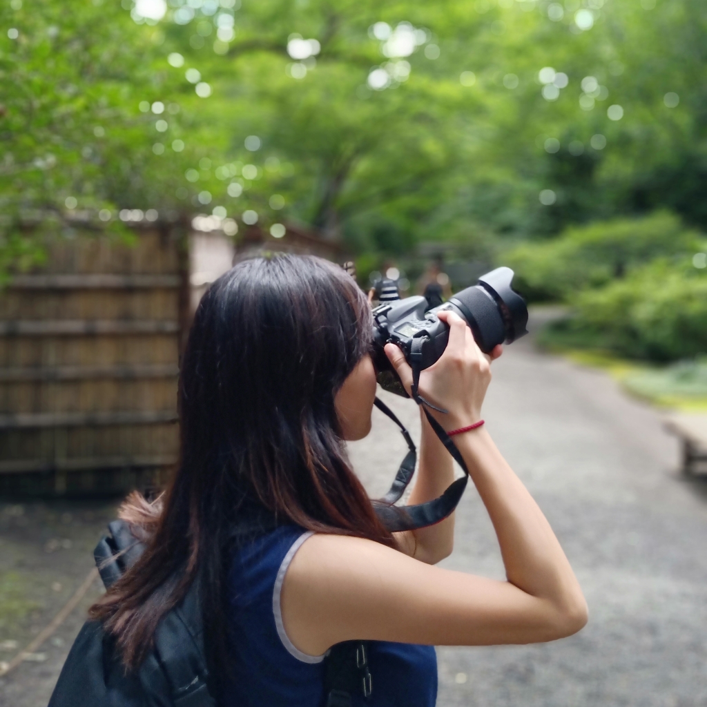 Back profile of a woman holding up a camera to her eyes in a garden